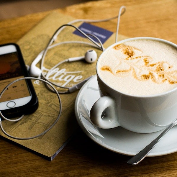 Mobiel met podcast ligt naast een kopje koffie