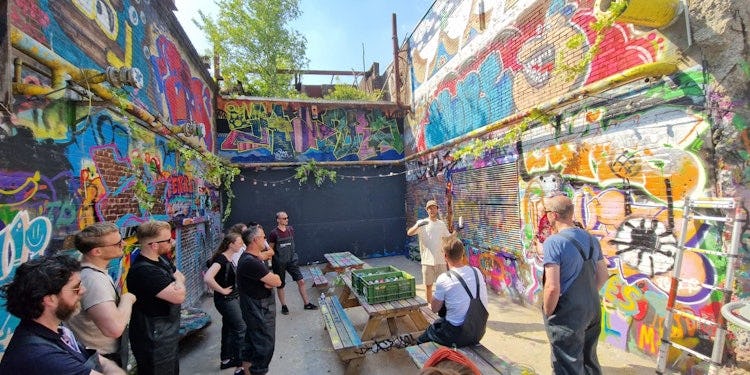 Medewerkers staan tussen twee muren vol spetterende graffiti en krijgen  uitleg over de workshop